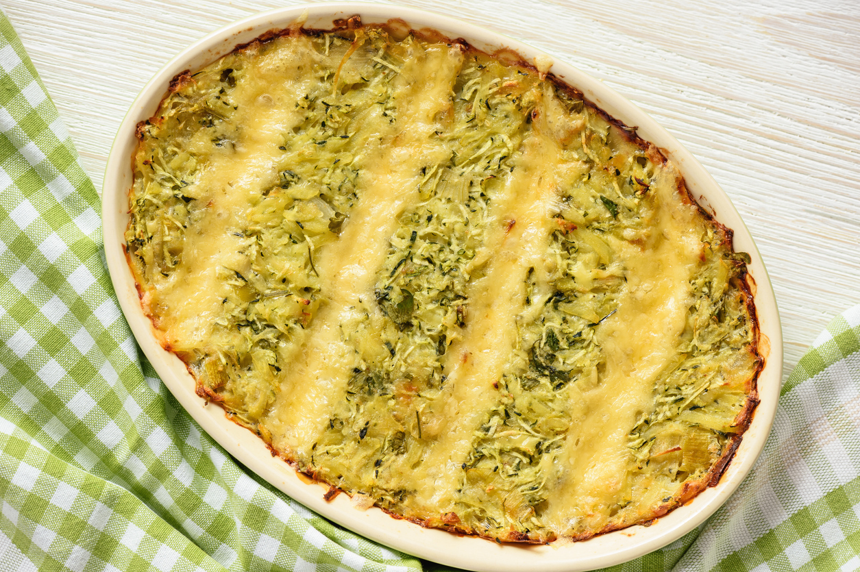 Zucchini-Kartoffel-Auflauf in ovaler Form, mit Käse überbacken, Draufsicht auf hellem Tisch.