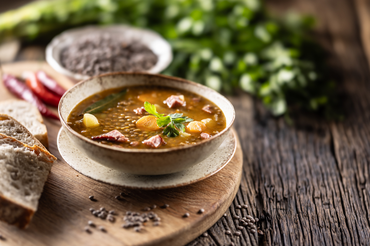 Linsensuppe mit Gemüse und Speck auf Holzbrett neben Brot