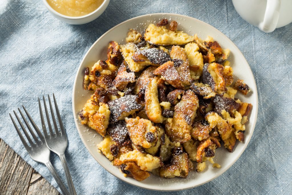 Goldbrauner Kaiserschmarrn auf Teller, mit Rosinen und Puderzucker.