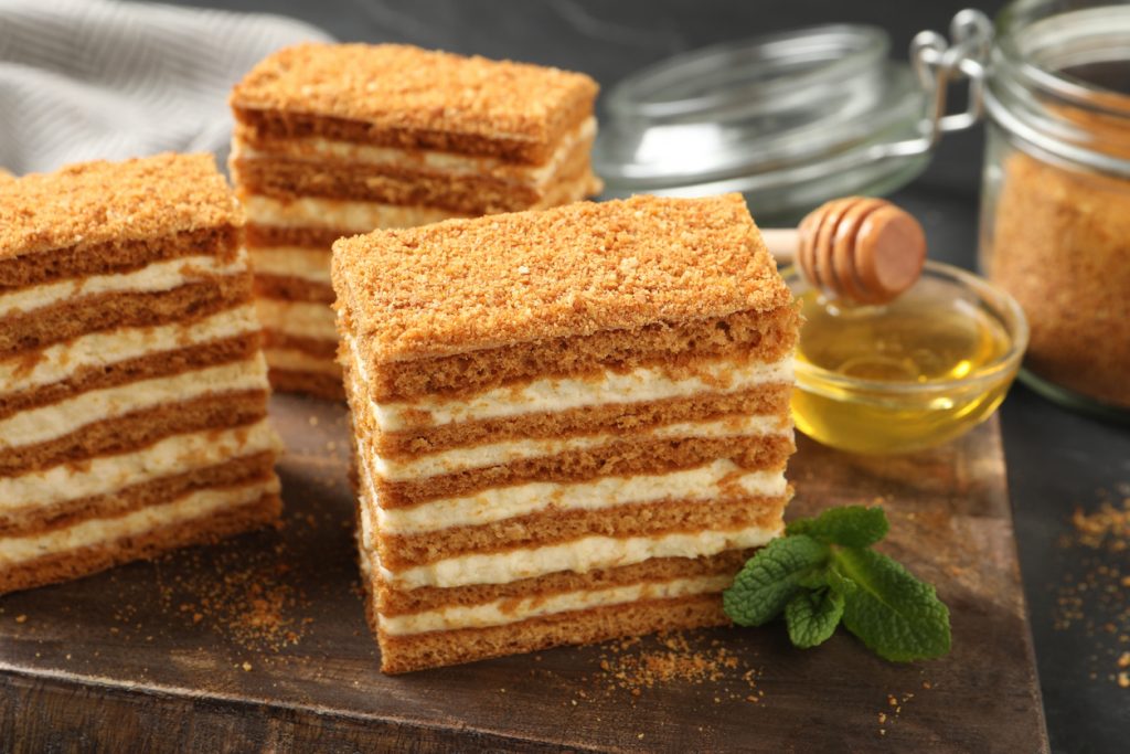 Mehrschichtiger Honigkuchen mit cremiger Füllung und Honig, serviert in rechteckigen Stücken.