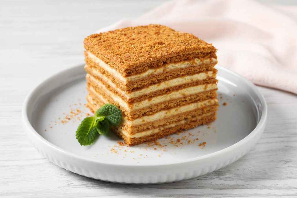 Quadratisches Stück Honigkuchen mit mehreren Schichten auf weißem Teller.