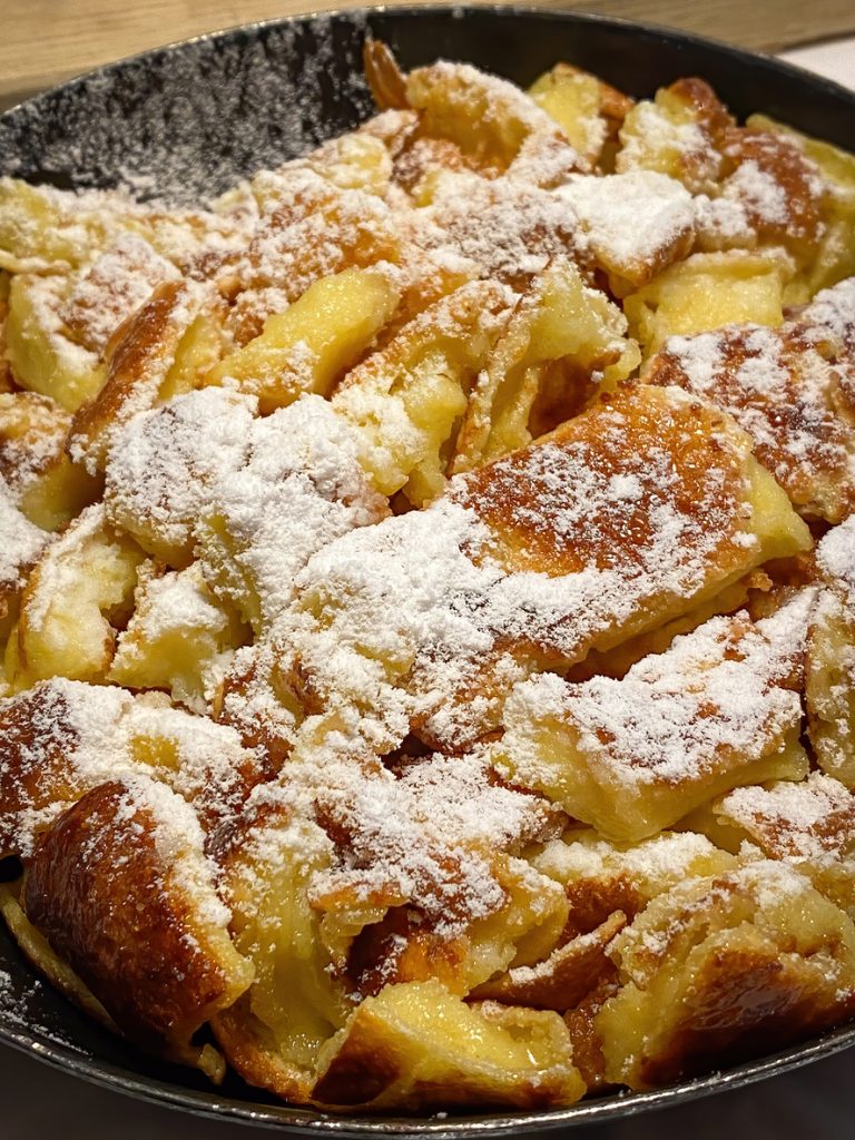 Goldbrauner Kaiserschmarrn in der Pfanne, großzügig mit Puderzucker bestäubt.