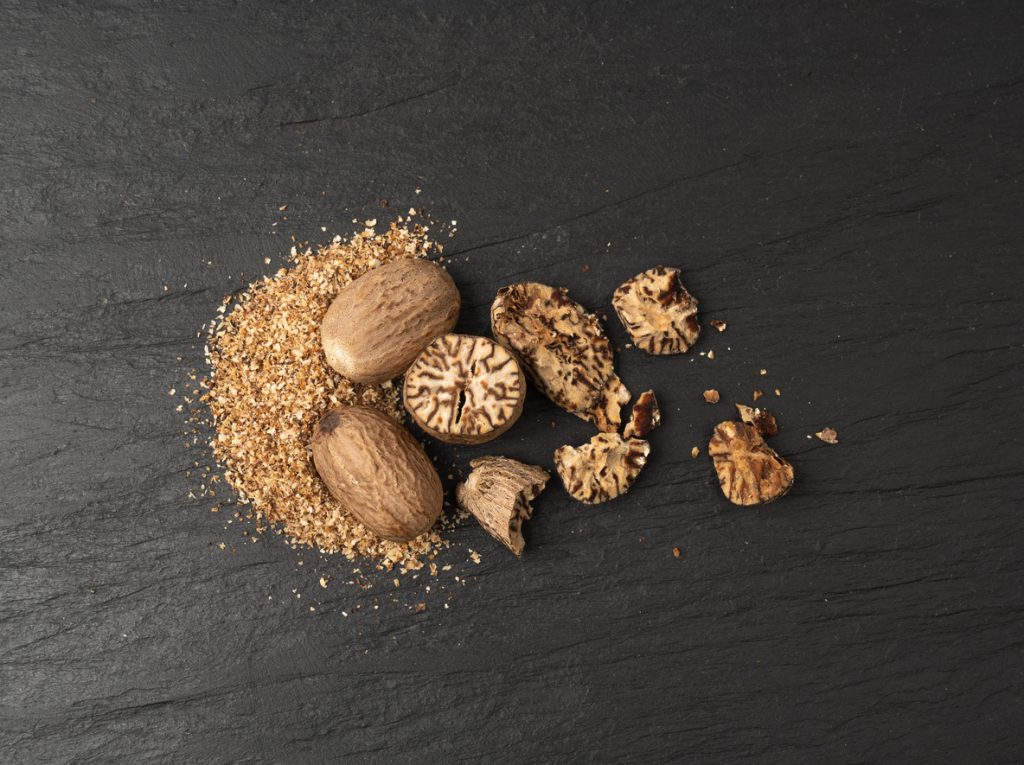 Muskatnüsse, Späne und Stücke liegen auf dunkler Schieferplatte.