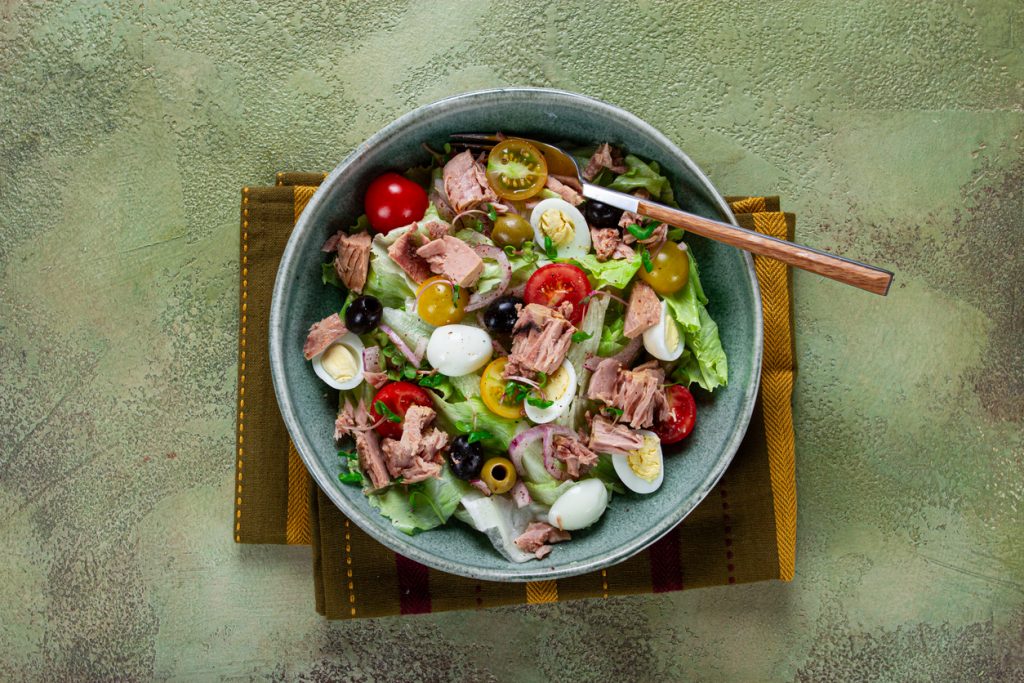 Schüssel mit Thunfischsalat aus Blattsalat, Kirschtomaten, Oliven, Zwiebeln und kleinen Eiern.