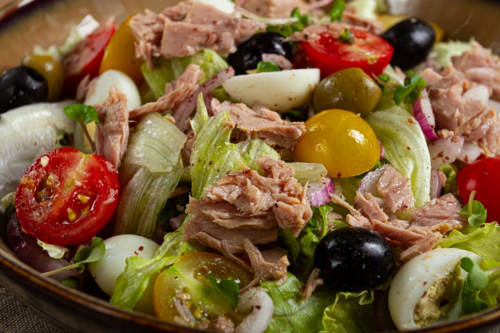 Nahaufnahme eines gemischten Thunfischsalats mit Eisbergsalat, Kirschtomaten, Eiern sowie schwarzen und grünen Oliven.