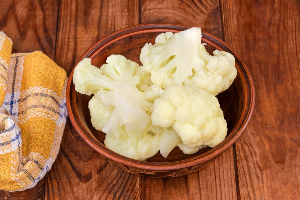 Schüssel mit blanchierten Blumenkohlröschen neben gelbem Küchentuch.