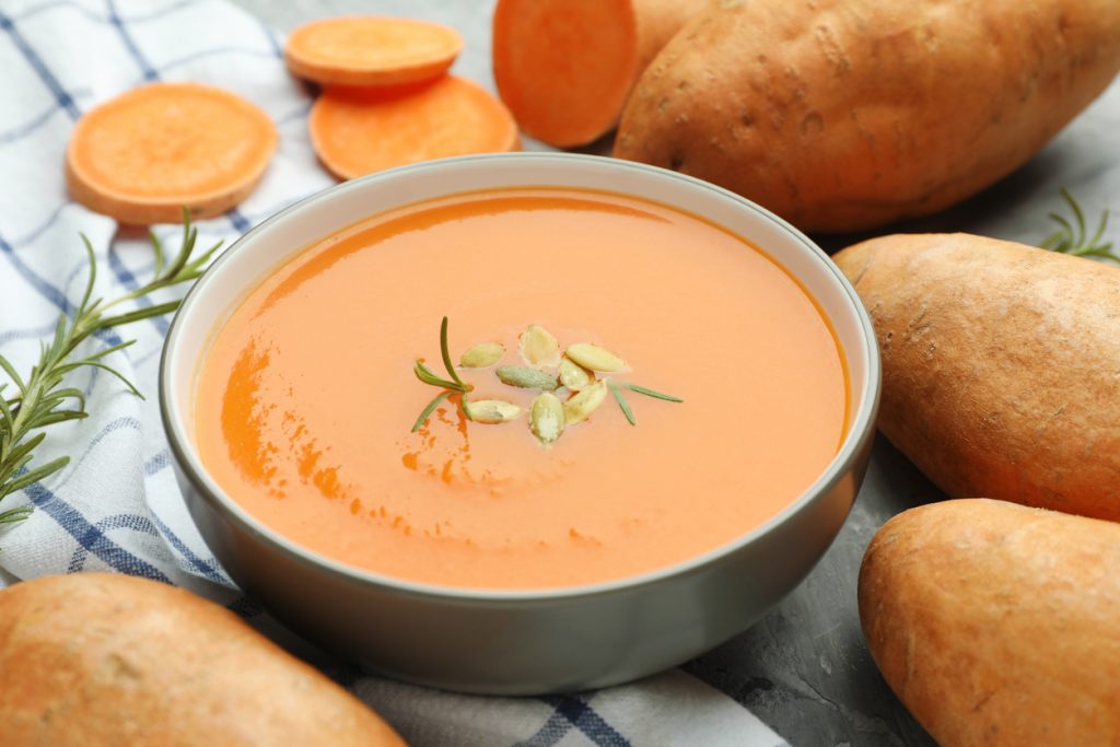 Schüssel mit cremiger Süßkartoffelsuppe, garniert mit Kernen und Rosmarin.