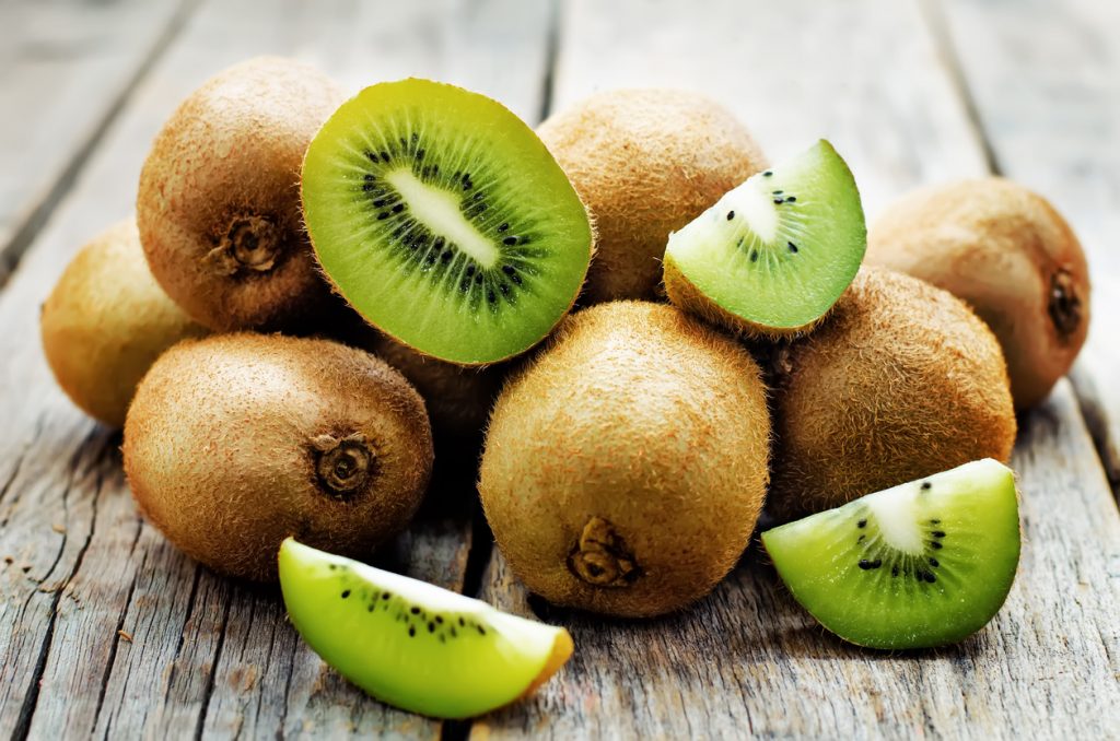 Ganze Kiwis liegen auf Holz, dazu halbe und geviertelte Stücke.