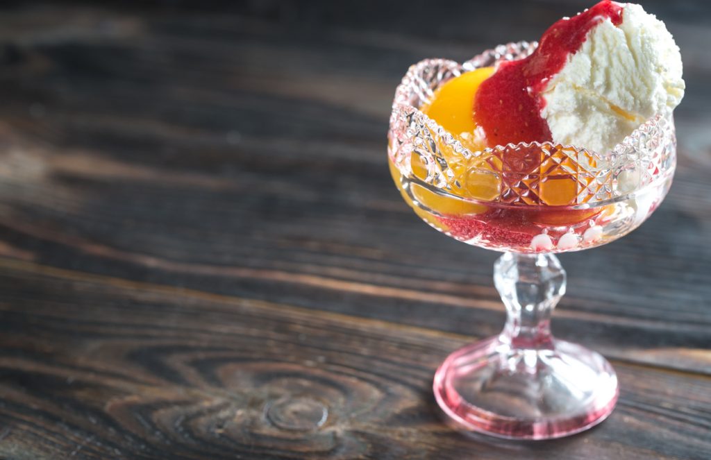 Pfirsichhälfte mit Vanilleeis und roter Himbeersauce in einem Dessertglas.