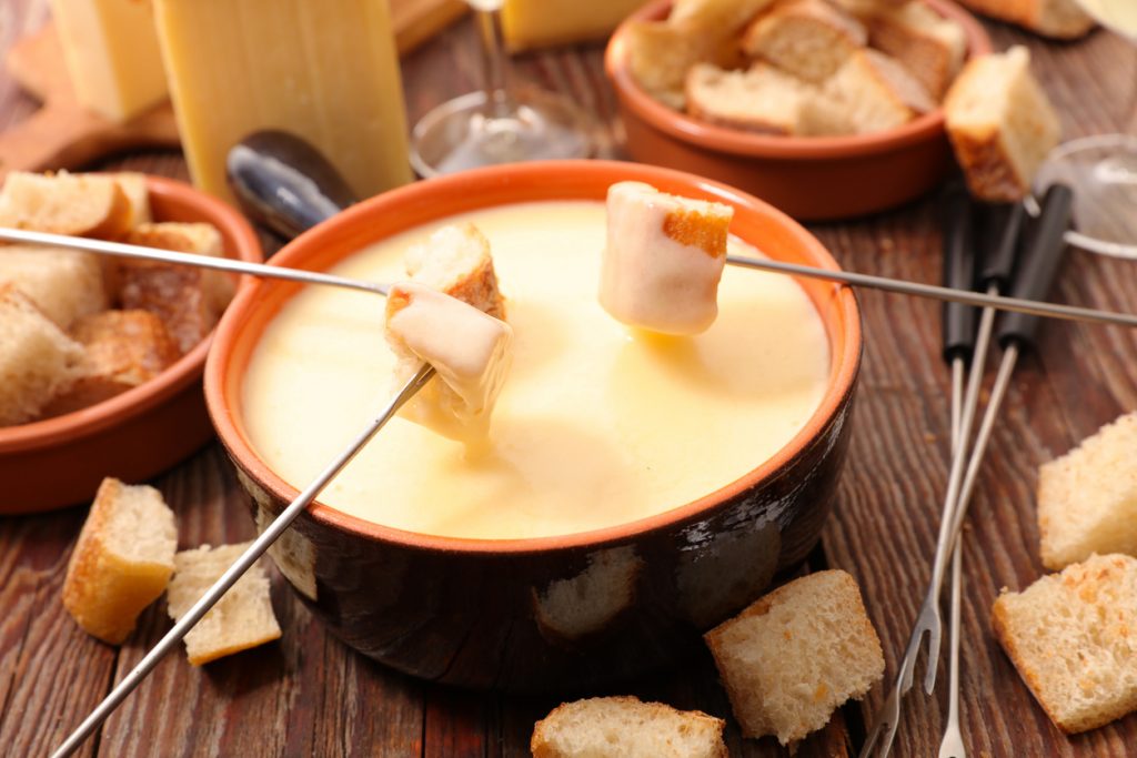 Cremiges Käsefondue im Topf mit Brotwürfeln auf Fonduegabeln.