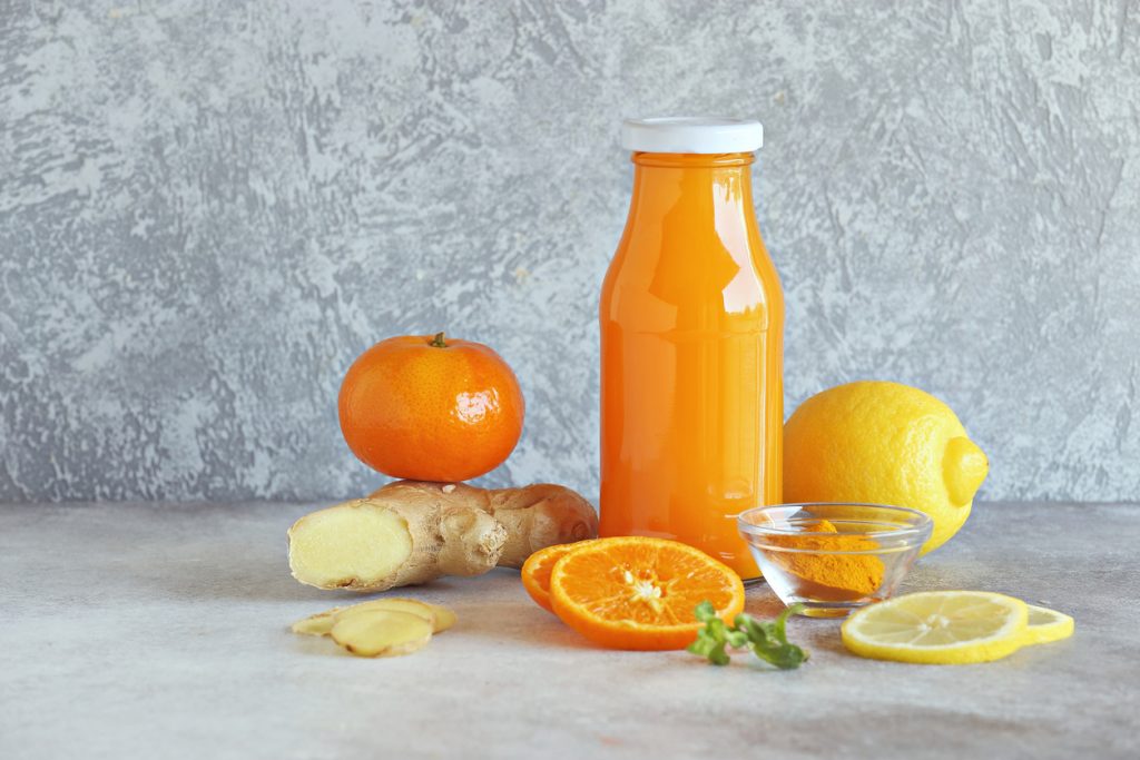 Flasche mit orangefarbenem Ingwer-Shot, Ingwerwurzel, Mandarine, Zitrone und Kurkumapulver.