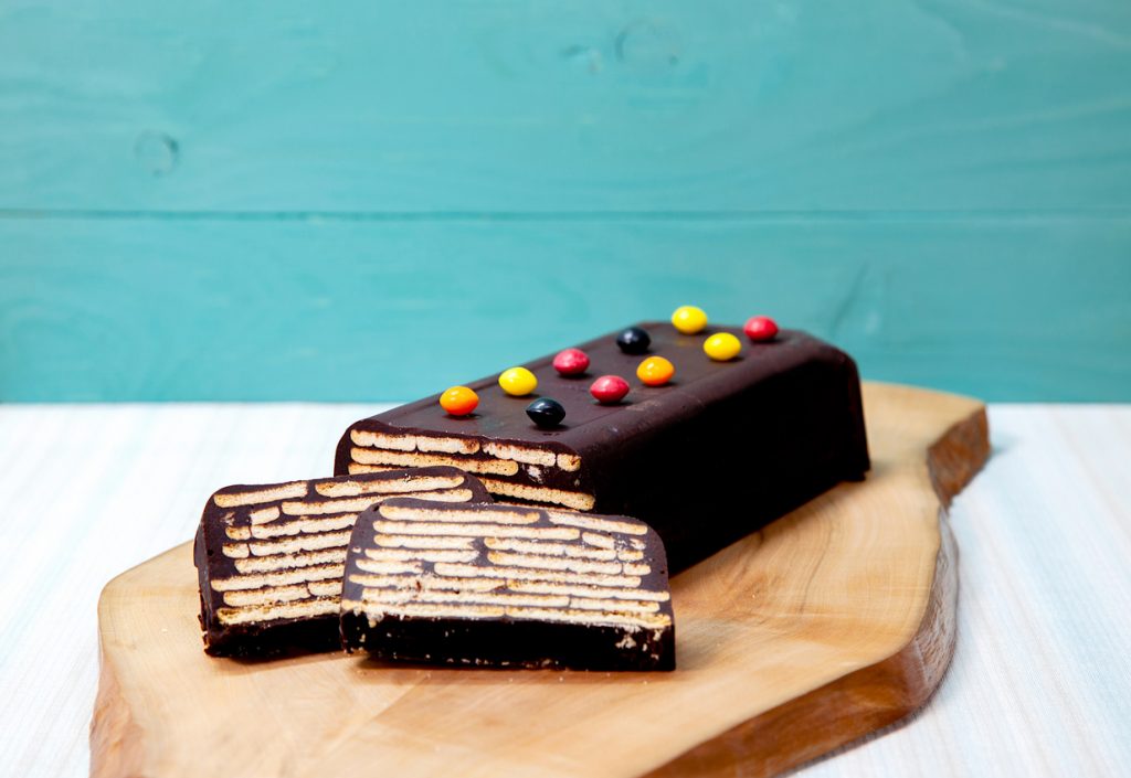 Schokokuchen mit Butterkeks-Schichten und bunten Schokodragees, vorne zwei Scheiben.