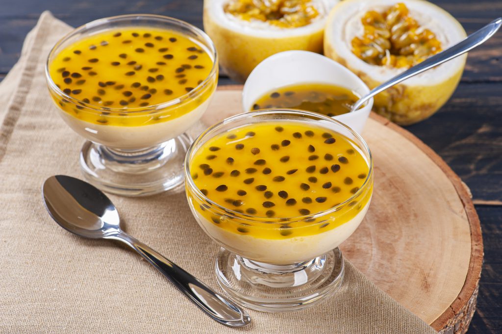 Zwei Dessertschalen mit gelber Passionsfruchtsauce und schwarzen Kernen auf Holz.