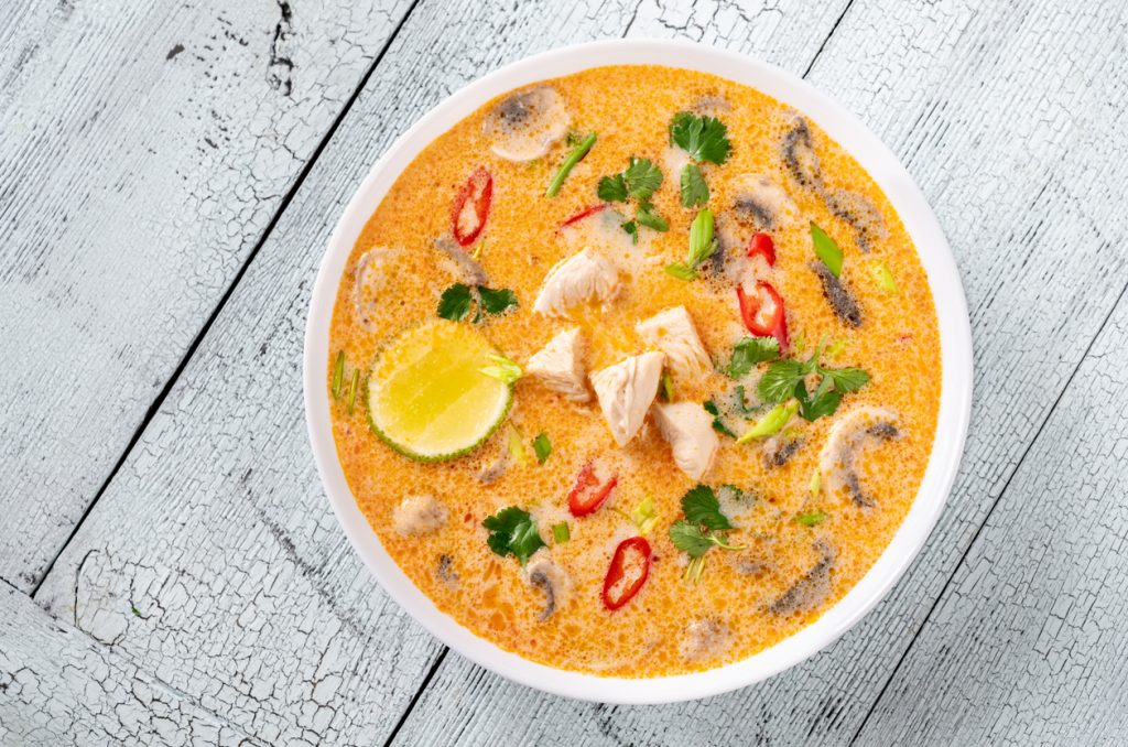 Weiße Schüssel mit Kokos-Hühnersuppe, Pilzen, Chili, Koriander und Limettenspalte.