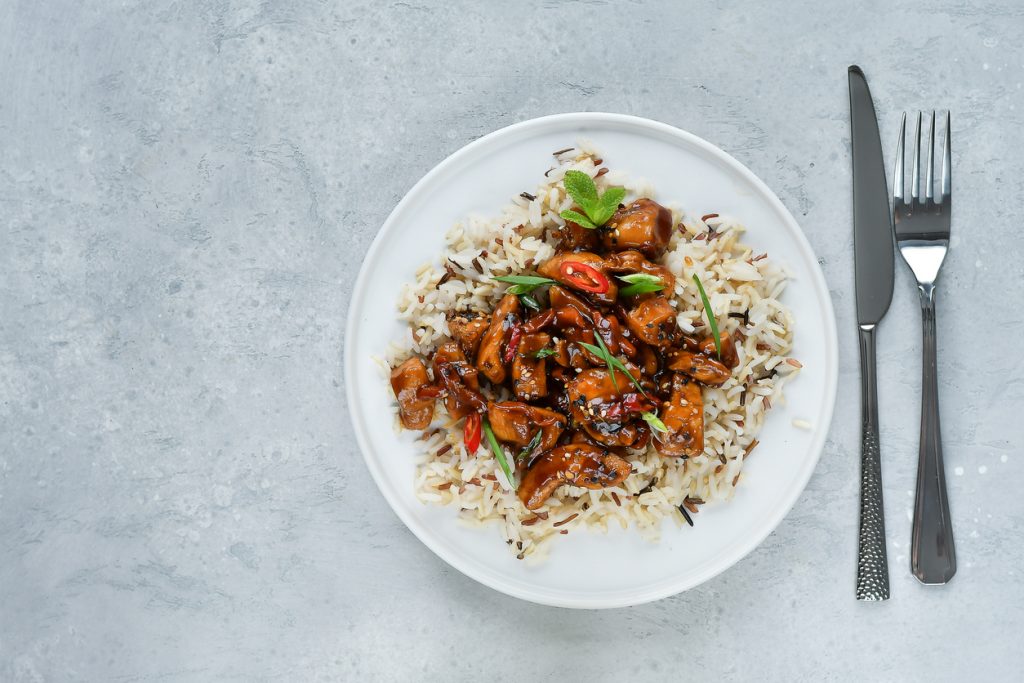 Weißer Teller mit Wildreis und glasiertem Teriyaki-Hühnchen, garniert mit Sesam und Chili.