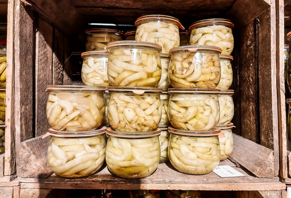 Mehrere Weckgläser mit geschnittenen Senfgurken stehen in einem Holzregal.