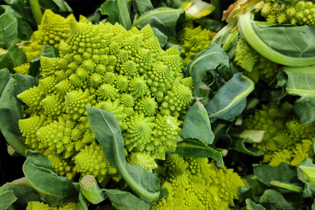 Mehrere Romanesco-Köpfe liegen mit Blättern in einer Auslage.