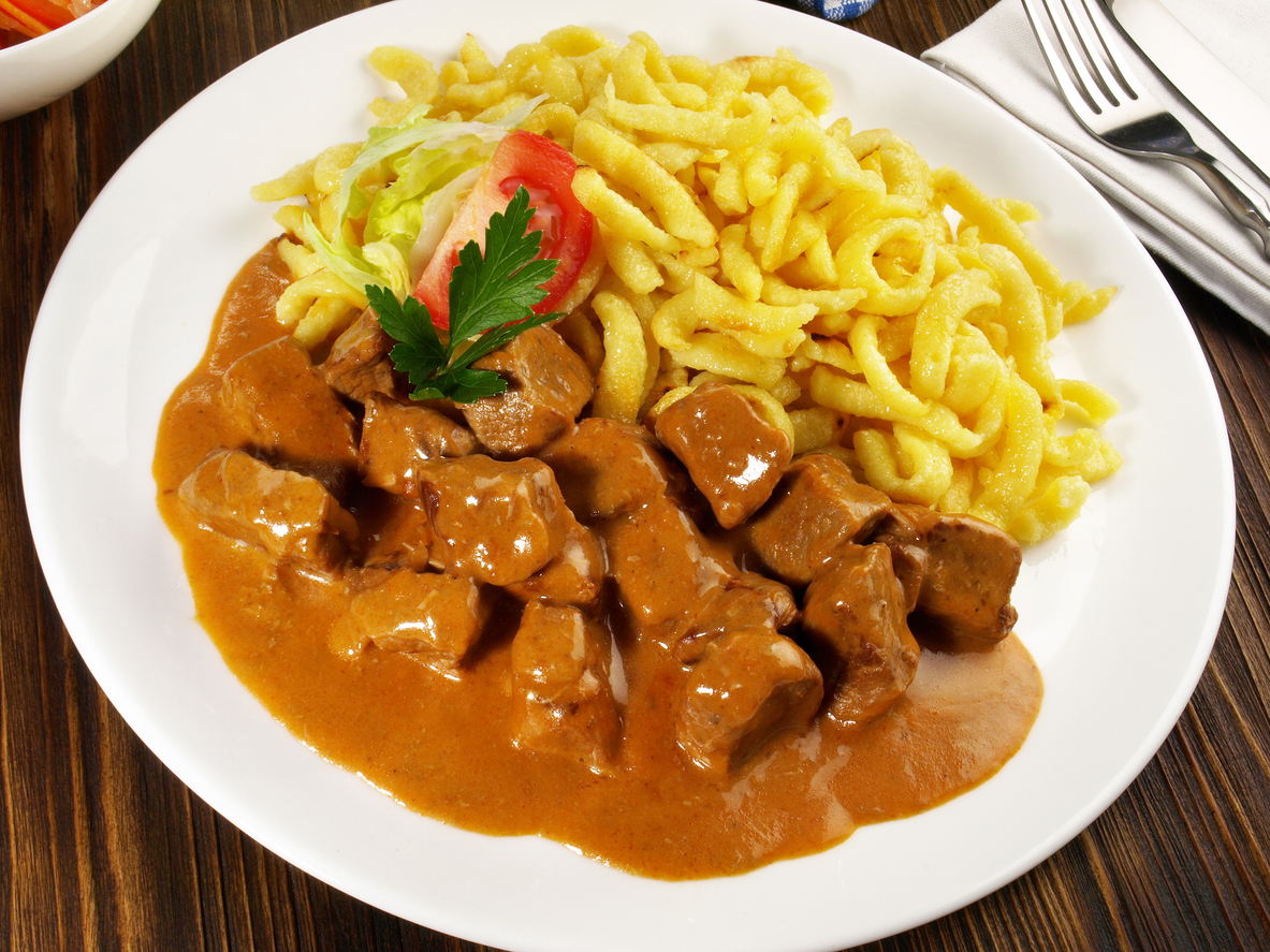 Teller mit Kalbsgulasch in brauner Sauce und Spätzle, mit kleiner Salatgarnitur.