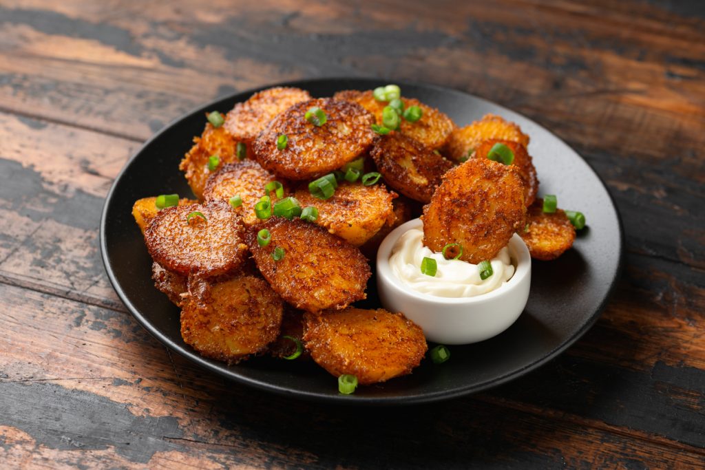 Scheiben von Babykartoffeln mit Parmesankruste auf schwarzem Teller mit Dip.