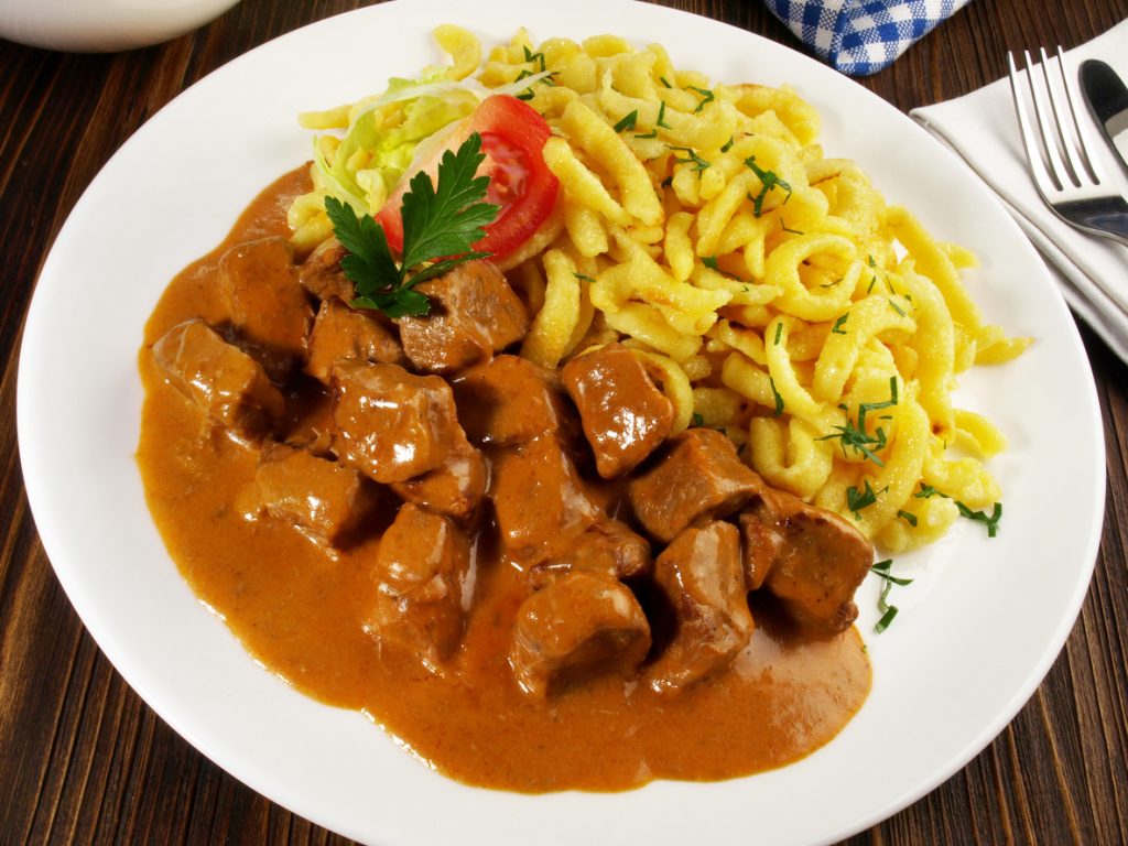 Weißer Teller mit Kalbsgulasch in sämiger Sauce und Spätzle mit Kräutern.