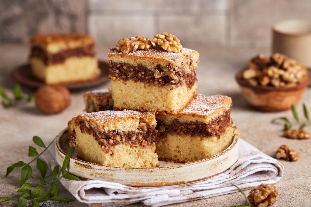 Mehrere gestapelte Kuchenwürfel mit nussiger Zimtschicht und Puderzucker.