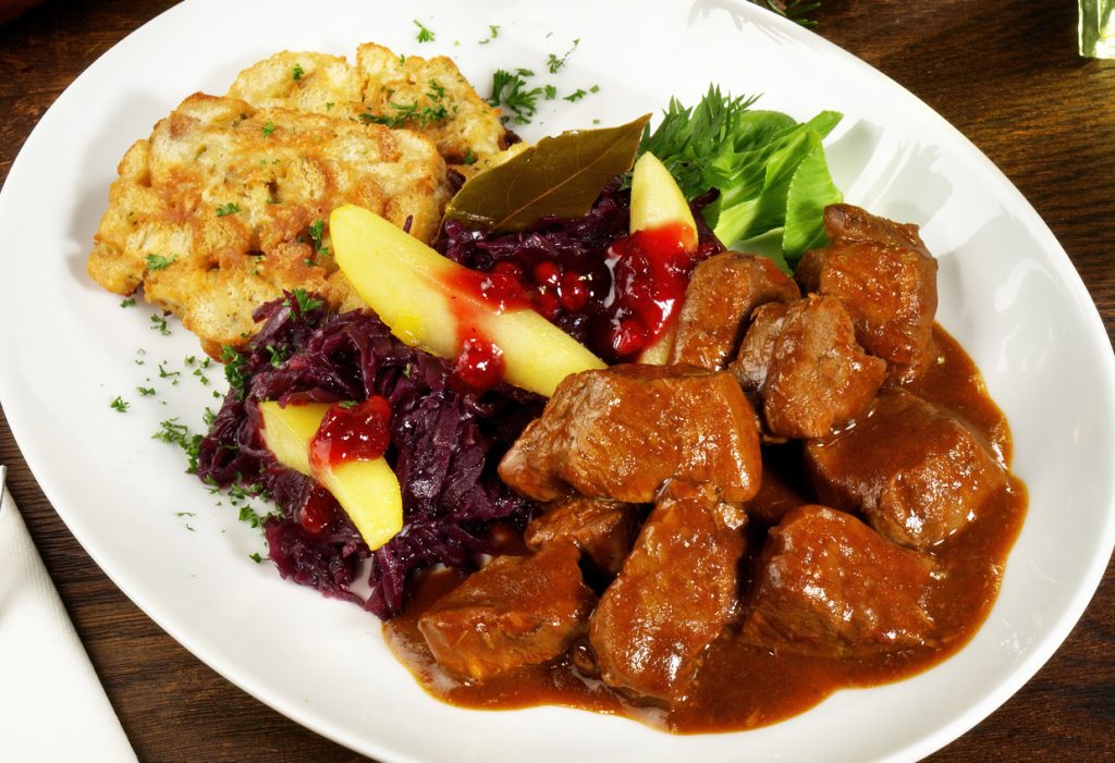Obere Ansicht von Hirschragout in Sauce mit Rotkohl, Apfelspalten, Preiselbeeren und gebratener Semmelknödelscheibe.