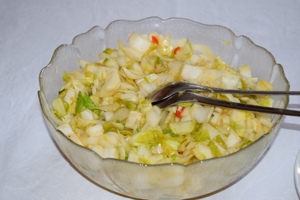 Kleingeschnittener Chicorée mit Dressing und etwas Paprika in einer Schüssel mit Besteck.