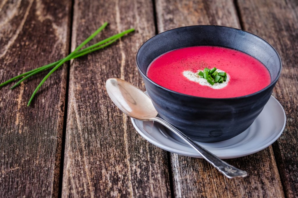 In einer schwarzen Schale liegt leuchtend pinke Rote-Bete-Suppe mit Joghurtstreifen und Schnittlauchröllchen.