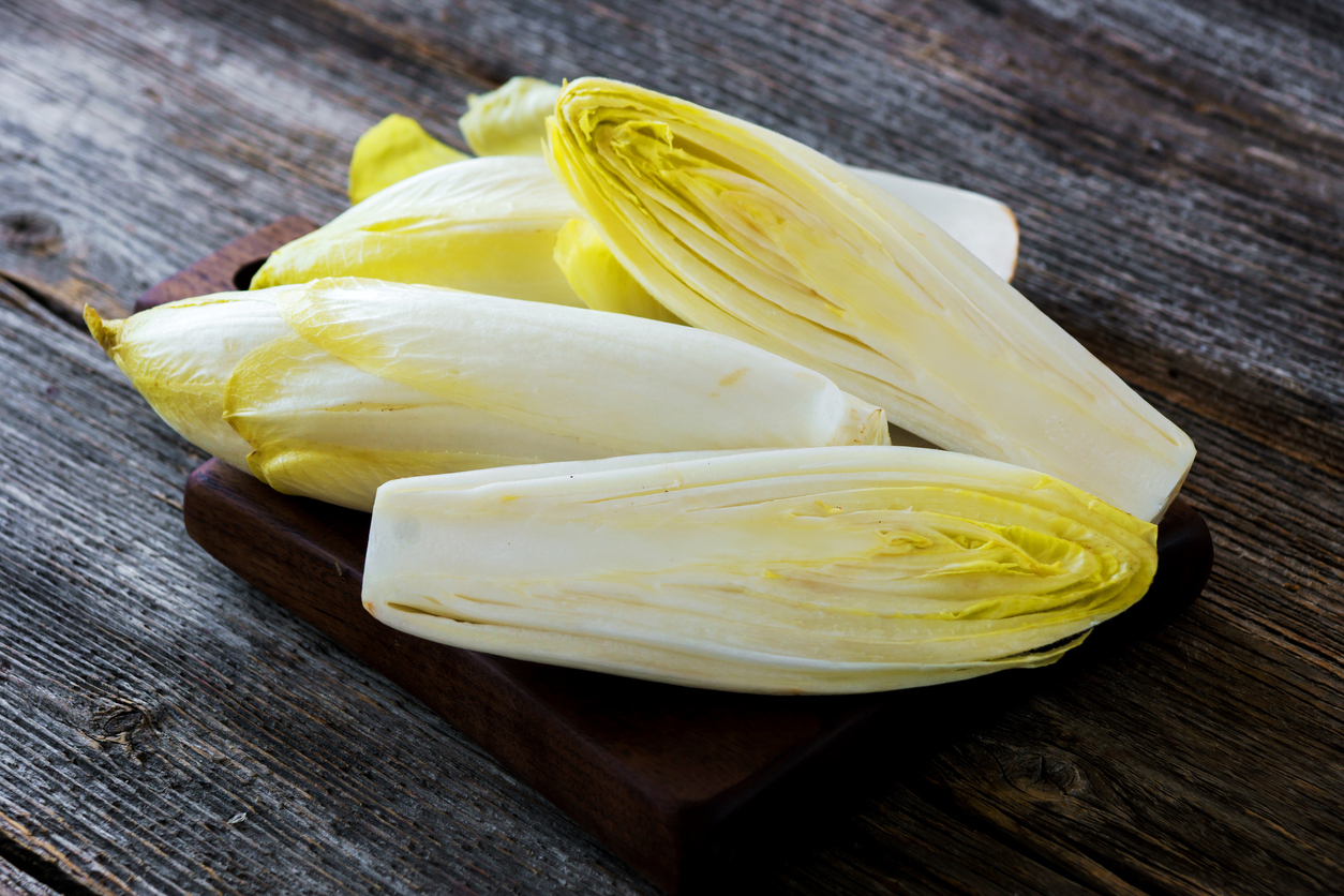 Mehrere helle Chicoréehälften auf einem Holzbrett.