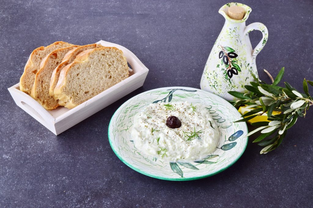 Teller Tzatziki mit Olive und Dill neben Brotscheiben und Ölkaraffe