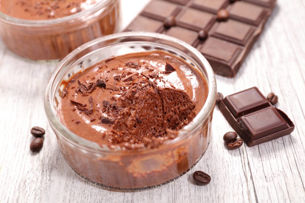 Glas mit Mousse steht neben Schokoladentafel und Kaffeebohnen.