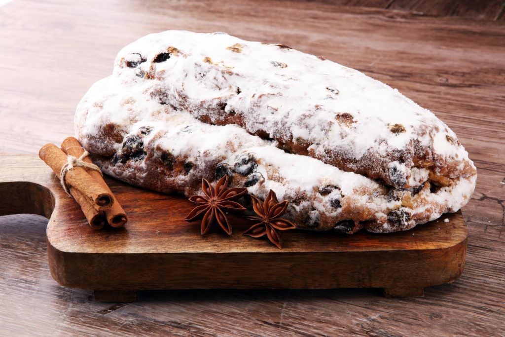 Ein ganzer, dick bepuderter Stollen liegt auf einem Holzbrett mit Zimtstangen und Sternanis.