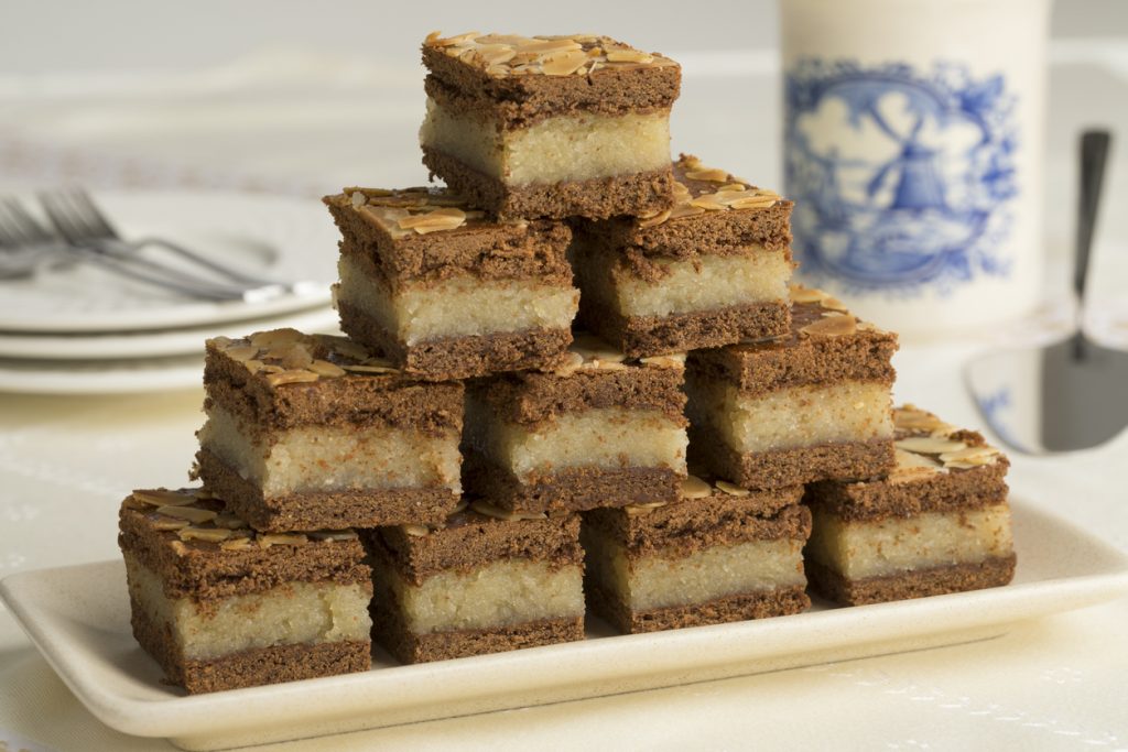 Mehrere kleine Würfel Gevulde Spekulatius mit heller Mandel-Füllung sind pyramidenförmig auf einem Teller gestapelt.