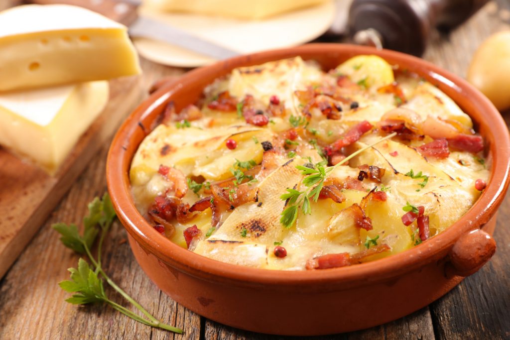 Tartiflette in einer braunen Auflaufform mit gebackenen Kartoffeln, Speck und geschmolzenem Käse.