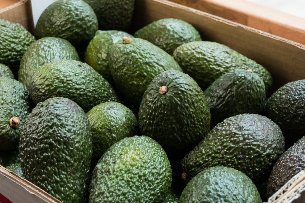 Mehrere Avocado-Früchte liegen dicht an dicht in einer Holzkiste.