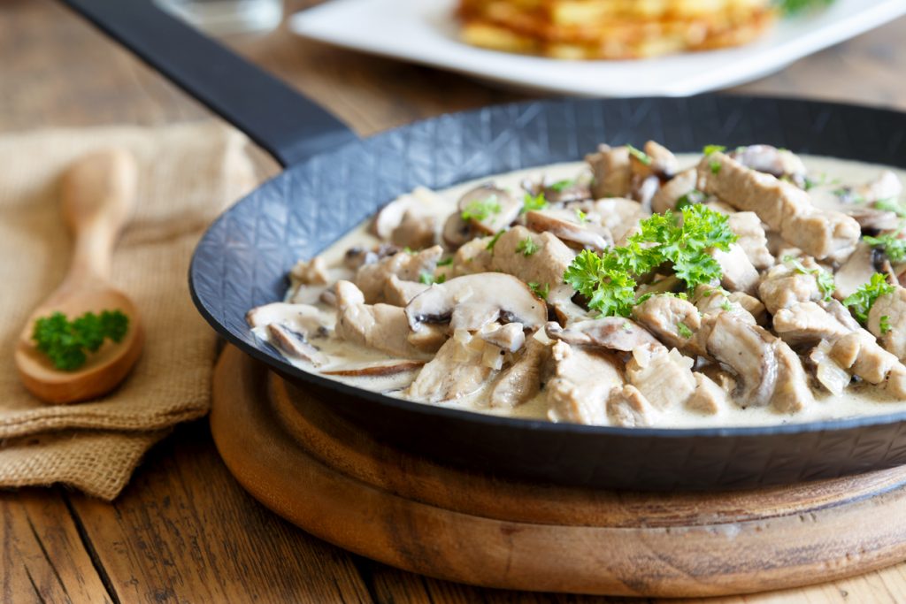 Züricher Kalbsragout mit Pilzen und Kräutern köchelt in einer großen Pfanne in cremiger Soße.