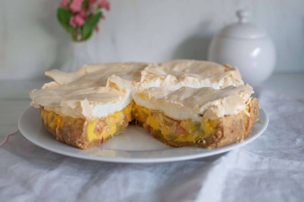 Eine runde Torte mit Baiserhaube steht angeschnitten auf einem weißen Teller.