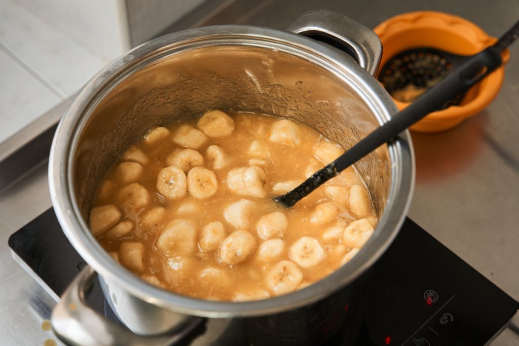 Bananenscheiben köcheln in einem Edelstahltopf als Grundlage für Bananenpudding mit Sahne und Keksschichten.