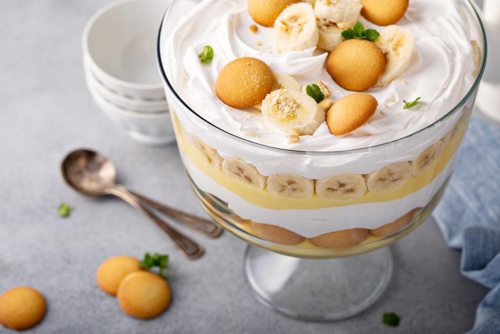 Nahaufnahme von Bananenpudding mit Sahne und Keksschichten mit Keksen, Bananenstücken und Minze obenauf.