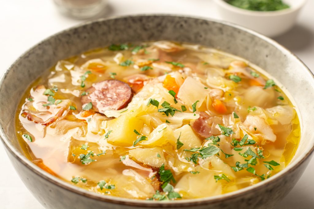 Polnische Sauerkrautsuppe Kapusniak mit Sauerkraut, Kartoffeln und Wurst in einer hellen Schale.