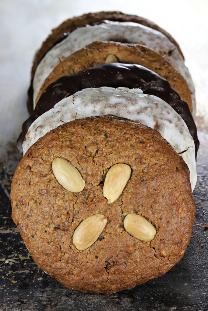 In einer Reihe aufgestellte Hausgemachte Lebkuchen, teils glasiert und teils schokoliert, liegen hintereinander auf dem Blech.