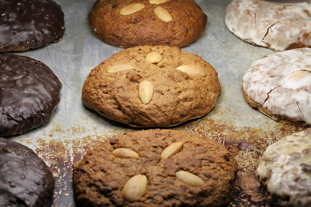 Mehrere Hausgemachte Lebkuchen mit ganzen Mandeln liegen dicht nebeneinander auf einem Blech.