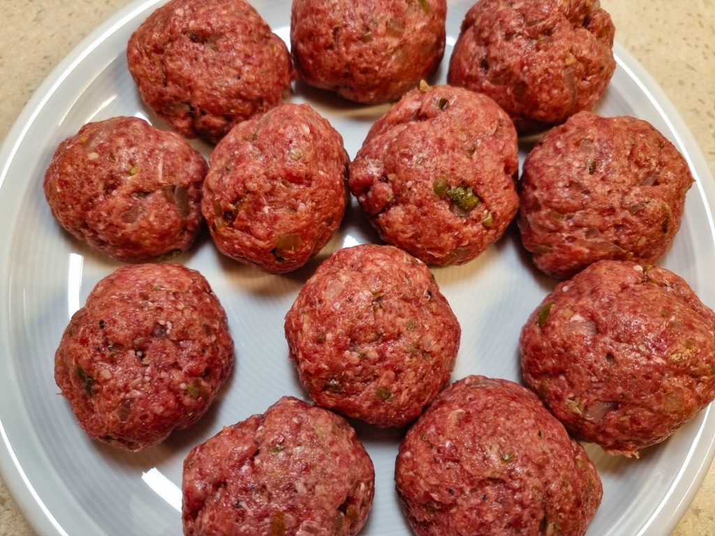 Geformte Königsberger Klopse aus Hackfleisch liegen roh auf einem Teller.