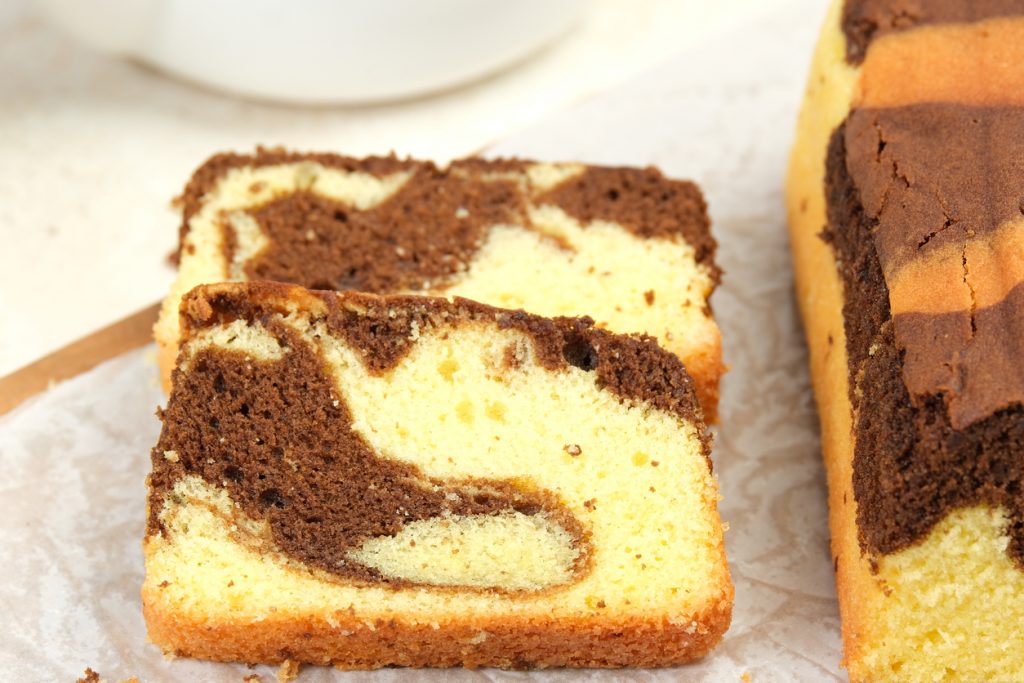 Mehrere Scheiben eines Marmorkuchens mit heller und dunkler Krume liegen nebeneinander auf Backpapier.