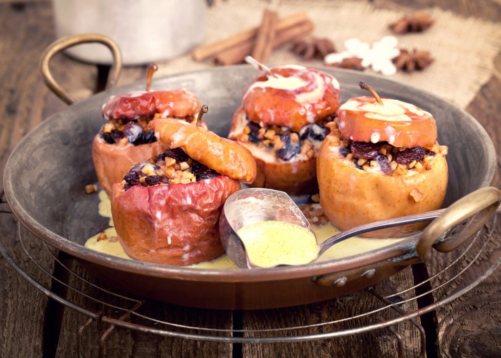 Mehrere gefüllte Äpfel in einer Metallform mit Soße und Löffel.