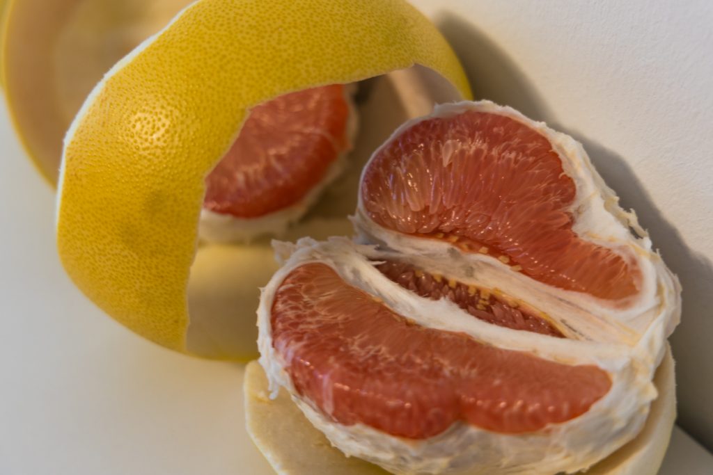 Halb geschälte Pomelo zeigt ihr saftig rotes Fruchtfleisch auf hellem Hintergrund.