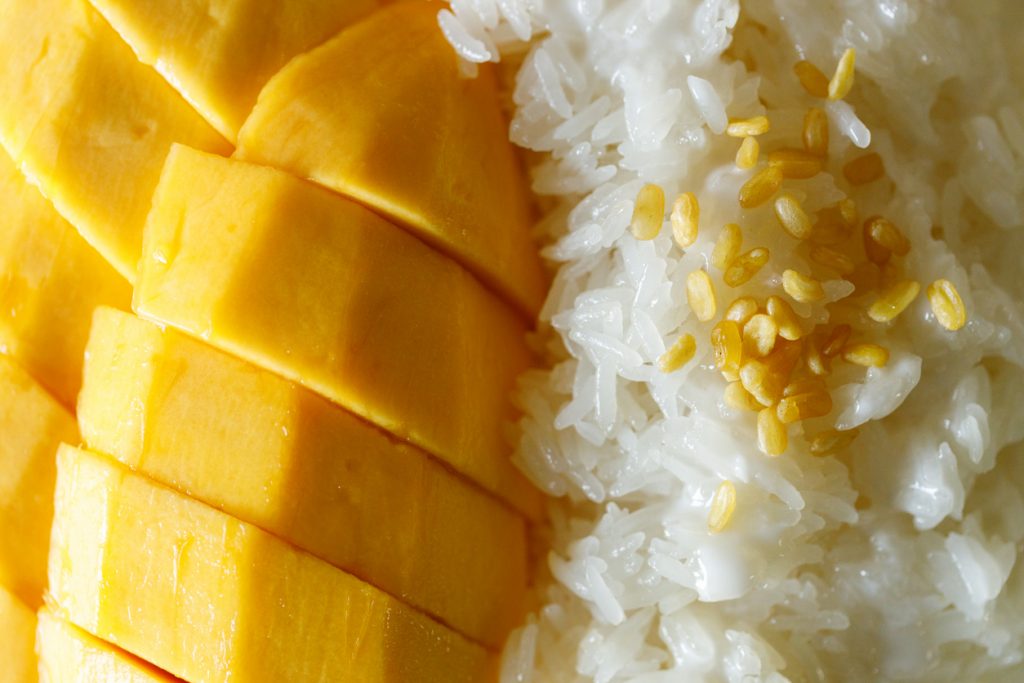 Nahaufnahme von Mango Sticky Rice mit Klebreis, Kokossauce und gerösteten Mungbohnen.