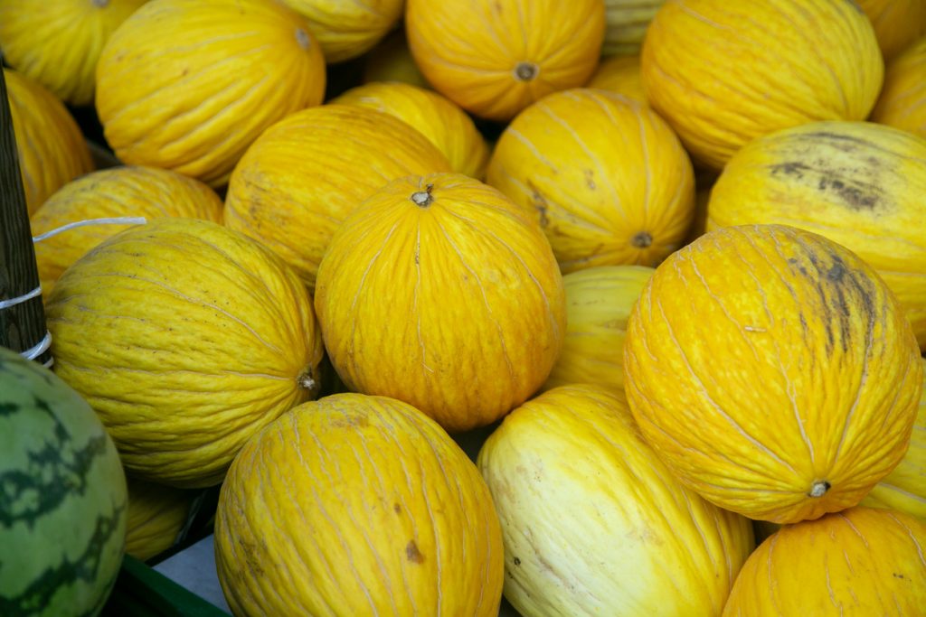 Mehrere ganze gelbe Honigmelonen liegen dicht aneinander in einer Auslage.