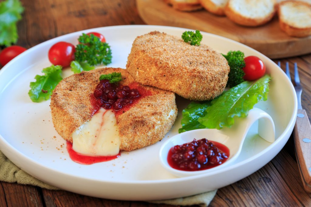 Gebackener Camembert auf einem weißen Teller mit Preiselbeeren, Salat und kleinen Tomaten.