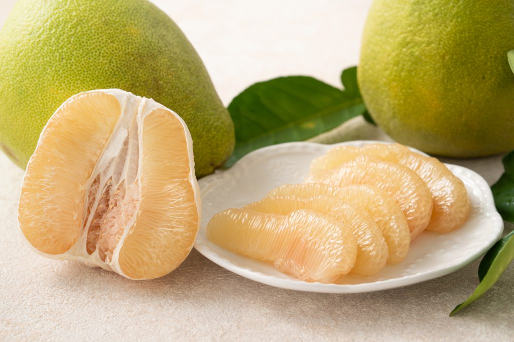 Halbierte Pomelo und geschälte Pomelo-Spalten liegen auf einem weißen Teller.